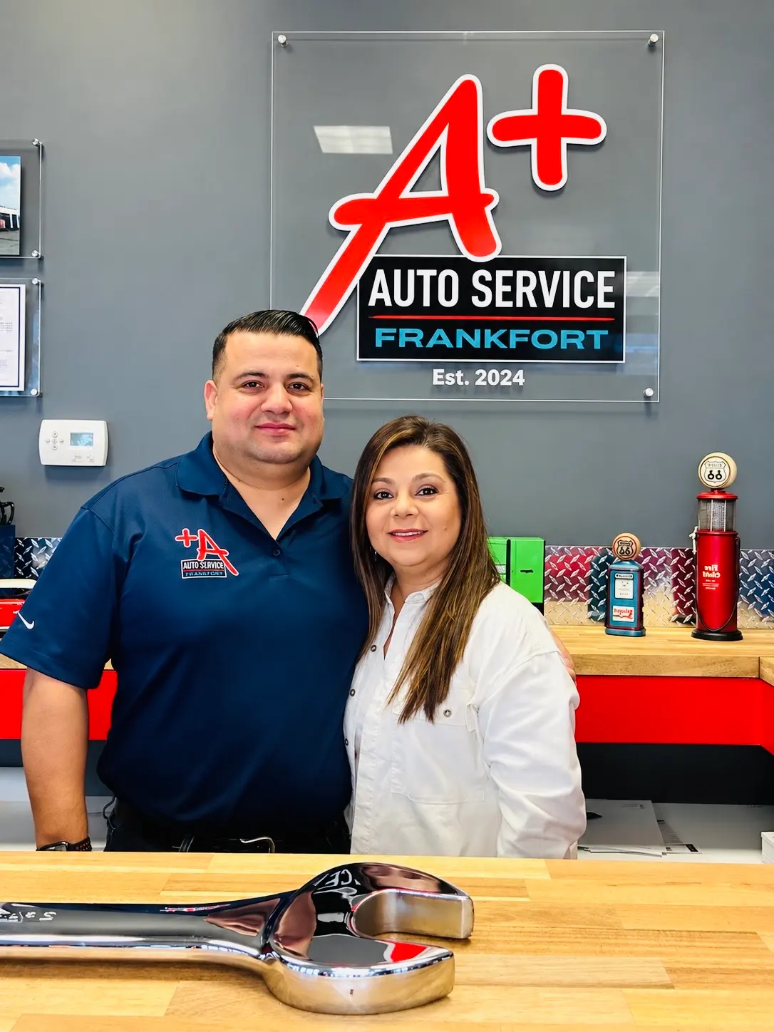 A Plus Auto Service owners Lina and Angel Herrera standing together at the Frankfort shop in front of the business logo